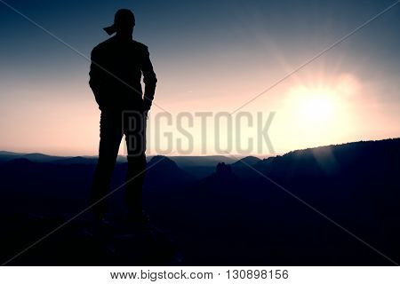 Hiker In Long Cap On Rock Empire And Watching To Sun. Beautiful Moment The Miracle Of Nature