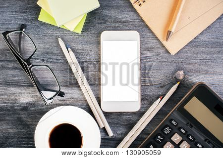 Top view of wooden desktop with blank white smart phone glasses coffee cup calculator and stationery. Mock up