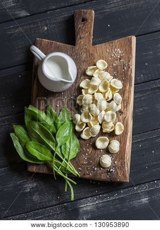 Raw ingredients for making pasta with spinach cream sauce - orecchiette pasta fresh spinach cream on a dark wooden background