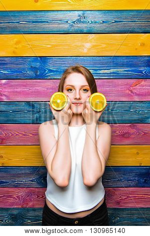 Young girl holds half of a juicy orange and smiles. Young girl on a colorful striped background. Fruit fashion girl. Full face. Bright juicy picture
