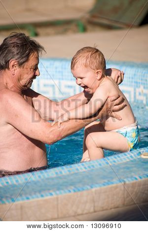 Farfar och barnbarn spelar tillsammans i poolen. Utomhus, sommar.