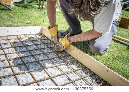 Closeup of a man making a net of steel bars by clipping them together with a wire and pliers placing it in as a reinforcement in a rectangular hole for a concrete foundation outside in backyard.
