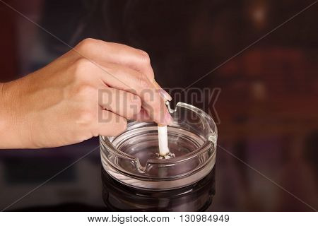 The female hand puts a cigarette in an ashtray on an abstract brown background.
