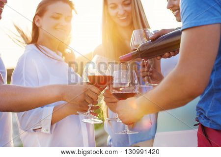 Group of happy friends having red wine on the beach. Sunset beach party