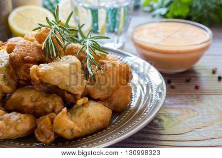 In the foreground shrimps in crispy dough on a plate with rosemary, in the background glass of water, lemon, herbs, bowl with sauce. Shrimps in pastry for lunch. Horizontal. Close.