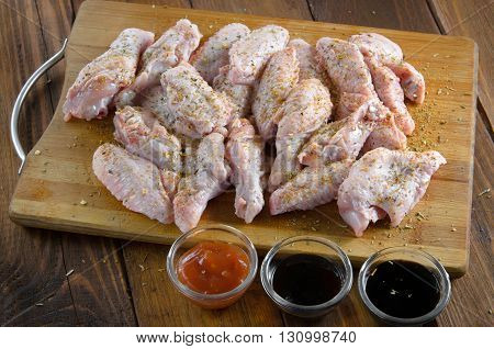 raw chicken wings with sauces on wooden table