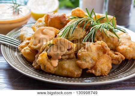 In the foreground shrimps in crispy dough on a plate with rosemary, in the background cutlery, glass of water, lemon, herbs and bowl with the sauce. Shrimps in pastry dressed with sauce. Horizontal.