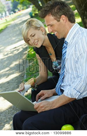 Giovani imprenditori seduto sulla panchina nel parco avendo luch e guardando il computer portatile.