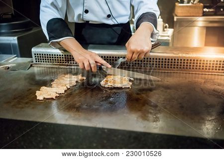 Hand Of Chef Cooking Chicken Steak On Hot Pan In Front Of Customers. Japanese Tepanyaki Steak