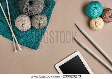 Grey And Turquoise Knitting Wool, Knitting Needles And A Tablet With A Black Screen On Beige Backgro