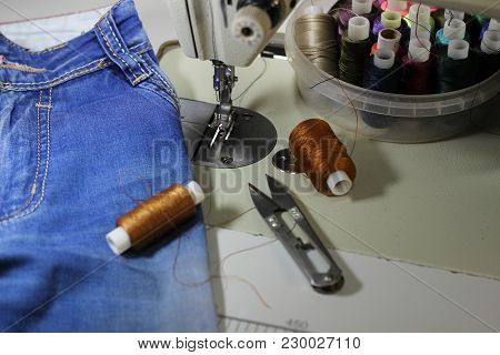 On The Table Of The Sewing Machine Lie Denim Fabrics, Close-up, Next To The Thread And Scissors.