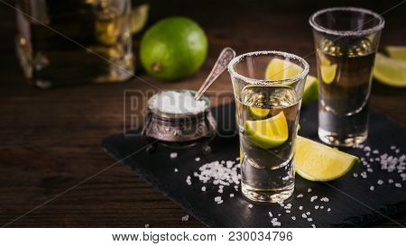 Gold Tequila Shot With Lime And Sea Salt On Black Table.