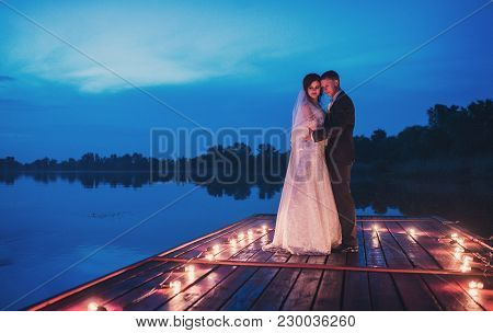 Night Wedding Ceremony. The Bride And Groom Hugging On Sea Pier