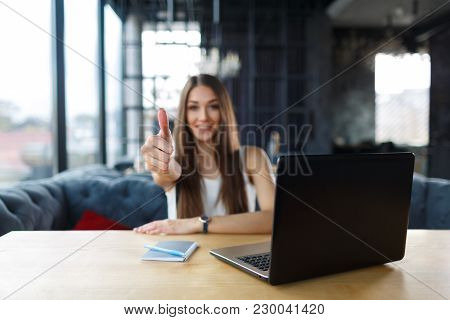 Young Woman Working On Her Laptop In The Restaurant. Smiling Beautiful Woman Showing Thumbs Up.