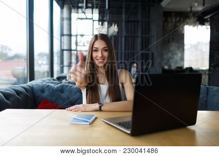 Young Woman Working On Her Laptop In The Restaurant. Smiling Beautiful Woman Showing Thumbs Up.