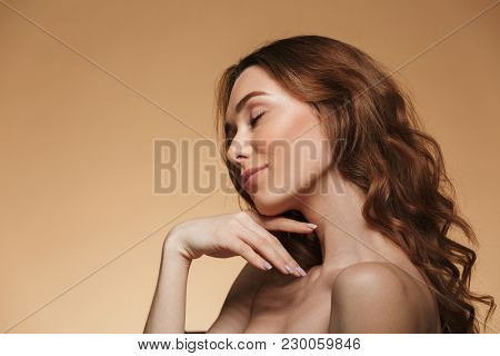 Photo in profile of half naked sensual lady 20s with natural makeup touching her neck with closed eyes isolated over beige background