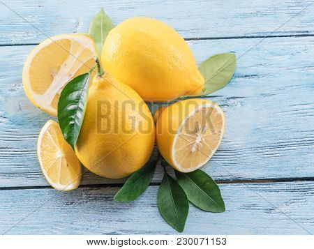 Ripe lemons and lemon leaves on blue wooden background. Top view.