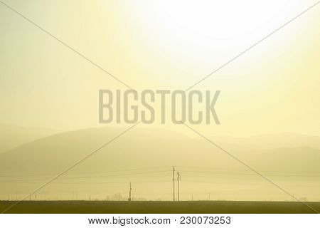 Panoramic View Of A Beautiful Sunrise In Golden Tones With Mountains In The Background And Some Pole