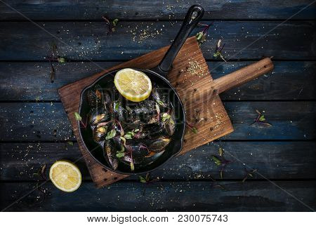 Delicious Mussels. Serving On A Hot Frying Pan With Herbs Spices And Lemon On A Colored Wooden Backg