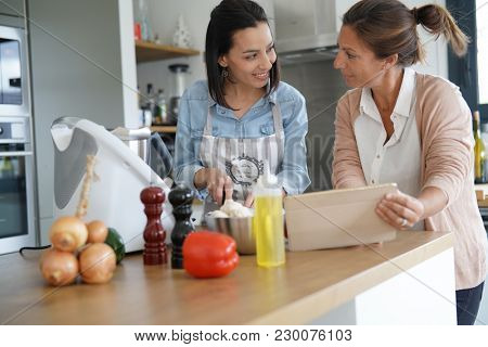 Friends cooking together with kitchen robot and tablet