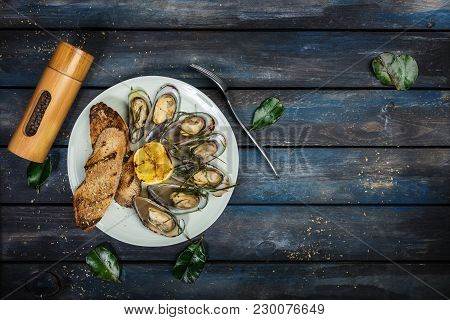 Mussels And Bread Toasts On On A White Plate. Served With Half Grilled Lemon, Fork And Leaves Of Kaf