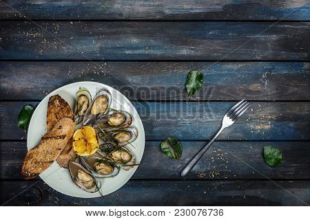 Mussels And Bread Toasts On On A White Plate. Served With Half Grilled Lemon, Fork And Leaves Of Kaf