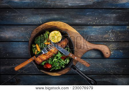 Grilled Salmon Fillet In A Frying Pan, Vegetables, Arugula With A Lemon Served With Cutlery. On The 