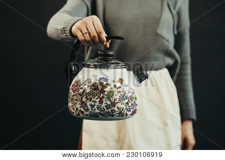 Woman Hand Holding Kettle On A Black Background.