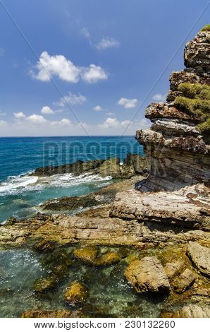 Rock With Amazing Texture Covered With Green Schrubs Facing The Ocean. Wave Hitting The Shore And Bl