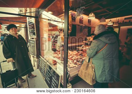 Munich, Germany - November 16, 2017: Senior Woman Buying Bacon And Sausage In A Meat Store At Viktua