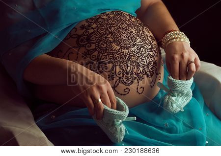 Mehendi artist paints an ornament of mandala with henna on an pregnancy woman’s belly