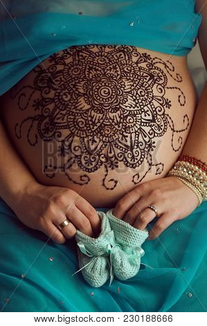 Mehendi artist paints an ornament of mandala with henna on an pregnancy woman’s belly