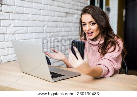 Beautiful Young Girl In Casual Clothes Is Using A Smart Phone And A Laptop, And Smiling While Sittin