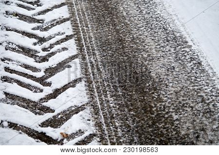 Tractor And Car Tracks In Snow On Winter Asphalt Road.