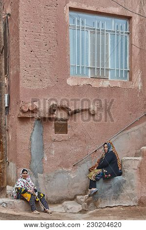 Abyaneh, Iran - April 26, 2017: Two Iranian Women In Hijabs Sit On The Stairs In The Countryside In 
