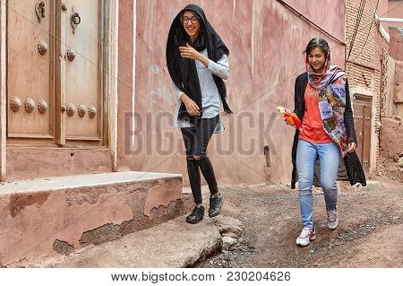 Abyaneh, Iran - April 26, 2017: Two Young Women In Hijabs Are Walking Along A Narrow Street In The T