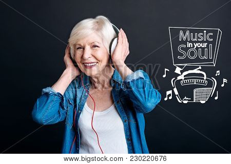 Loving Music. Happy Senior Woman Feeling Glad While Wearing Big Modern Headphones And Listening To P