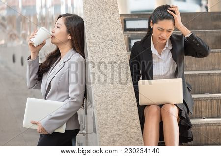 Asian Business Woman Stessing When Using A Laptop While Another Business Woman Who Hold A Laptop Sta