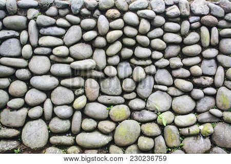 Exterior Pebble Stone Wall With Weed And Moss Grow On It. Texture Background.