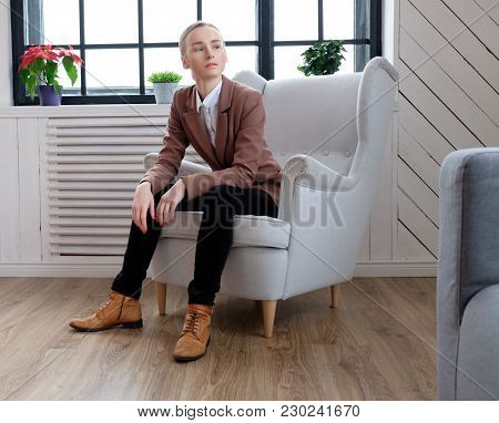 Casual Young Woman In A Brown Jacket Relaxing In A Room With Wondow.