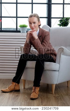 Casual Young Woman In A Brown Jacket Relaxing In A Room With Wondow.