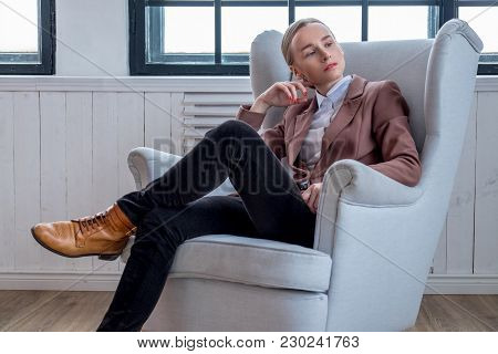 Casual Young Woman In A Brown Jacket Relaxing In A Room With Wondow.