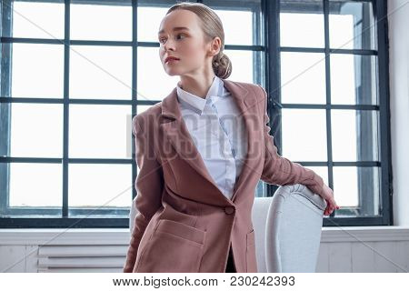Casual Young Woman In A Brown Jacket Relaxing In A Room With Wondow.
