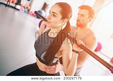 Close Up Of Young And Beautiful Boy And Girl Exercising In Gym. She Is Doing Some Squads Using Bodyb