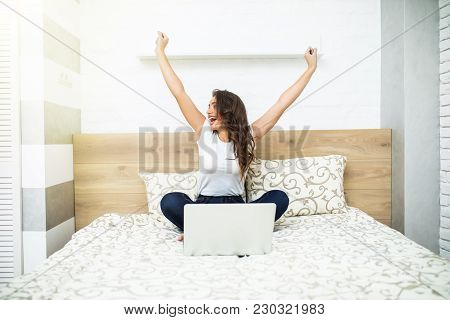 Girl With Raised Hands In Bed Using Laptop At Home