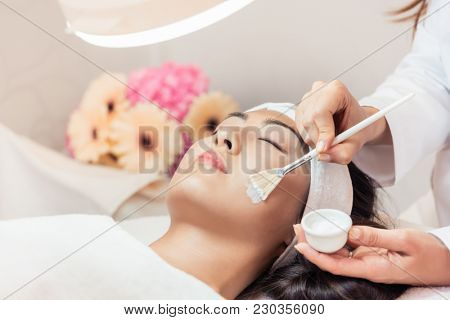 Close-up of the face of a beautiful young Asian woman relaxing during rejuvenating facial massage with brushes in a contemporary beauty center