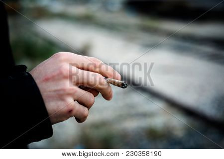 closeup of a young caucasian man outdoors smoking a hand-rolled cigarette or a joint
