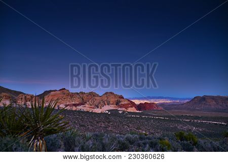 redrock canyon at night with las vegas nevada lit up behind rocks
