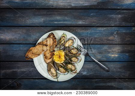 Mussels And Bread Toasts On On A White Plate. Served With Half Grilled Lemon And Fork. Wooden Backgr