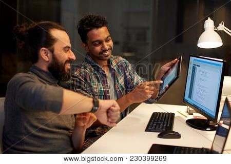 deadline, technology and people concept - creative team with tablet pc computer and smartwatch working together late at night office